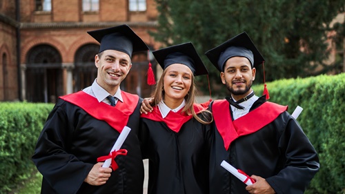 Portrait of three smiling graduate friends in graduation robes in university campus with diploma.